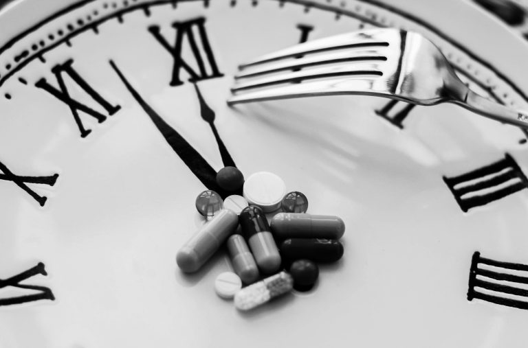 Horloge en noir et blanc avec des comprimés et gélules, illustrant la pression du temps et la charge de travail des jeunes médecins en début de carrière